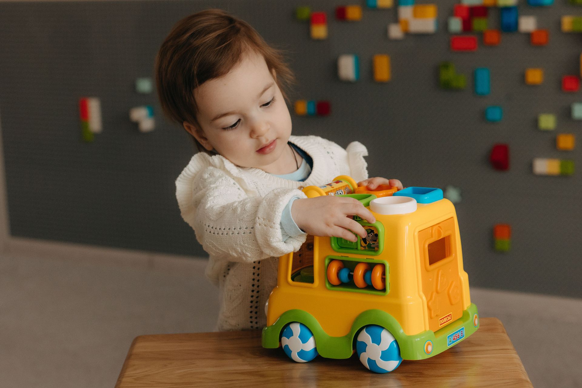 A young child playing with a colorful toy truck indoors, showcasing creativity and curiosity.